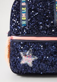 Marinblå sequinsryggsäck med rosa dragkedja, har en genomskinlig stjärnformad charm fylld med färgglada stjärnor och ett färgglatt textband.