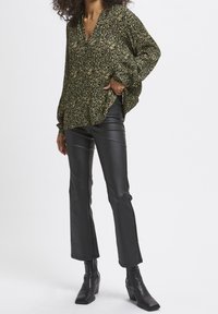 Blouse à motifs noir et jaune avec un décolleté en V, coupe loose et manches longues, associée à un pantalon évasé en simili cuir noir et des bottines.
