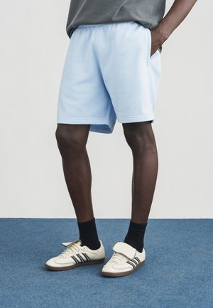 Pantaloncini di cotone azzurro chiaro con vita elasticizzata e tasche laterali, abbinati a sneaker bianche e nere con cinturino in velcro.