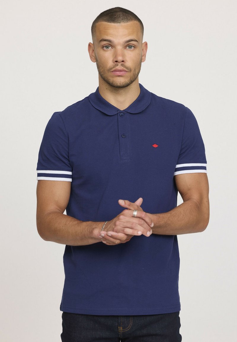 Polo shirt bleu marine avec un col classique, une patte de boutonnage à trois boutons, des manches courtes à rayures blanches et un petit logo rouge sur la poitrine.