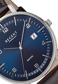Montre ronde en argent avec un cadran bleu foncé, des index horaires en argent, une fenêtre de date et un bracelet en cuir marron. Elle est dotée d'un verre saphir.