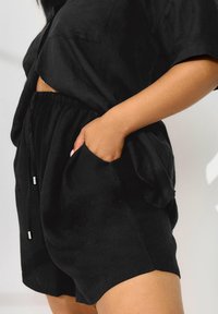 Ensemble en lin noir composé d'un haut surdimensionné avec une poche poitrine et d'un short taille élastique. Les shorts ont des poches latérales et une coupe décontractée.