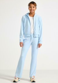 Jasnoniebieska bluza z kapturem na zamek z przednimi kieszeniami, zestawiona z dopasowanymi dresami. Miękka tekstura materiału i elastyczny pas ze sznurkiem do ściągania. Sneakersy w kolorze dopasowanym do stroju.