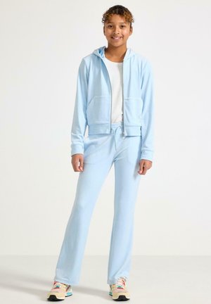 Lichtblauwe hoodie met rits en voorzakken, gecombineerd met bijpassende joggers. Zachte stoftextuur en elastische tailleband met trekkoord. Kleurenmatchende sneakers.
