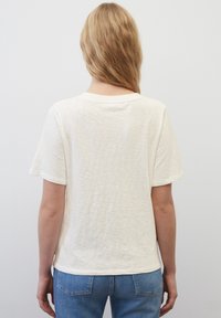 Kortärmad, krämfärgad T-shirt i mjukt, texturerat tyg med rund hals och avslappnad passform, kombinerad med ljusblå jeans.