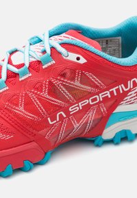 Scarpa da corsa rossa con tessuto in rete, accenti turchesi e branding bianco. Caratterizzata da una suola testurizzata con linguette prominenti per la trazione.