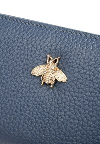 Borsa in pelle blu con texture, caratterizzata da un emblema d'ape tono oro come dettaglio decorativo. Il materiale ha una finitura a ciottoli.