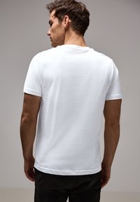 T-shirt bianco in cotone con maniche corte e colletto rotondo, caratterizzato da una texture liscia e un design retro semplice.