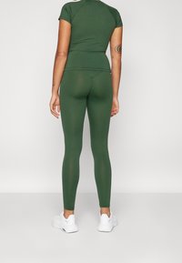 Zelený sportovní top a odpovídající legíny vyrobené z pružného materiálu. Bílé obuv. Oblečení má jednoduchý, přiléhavý design.