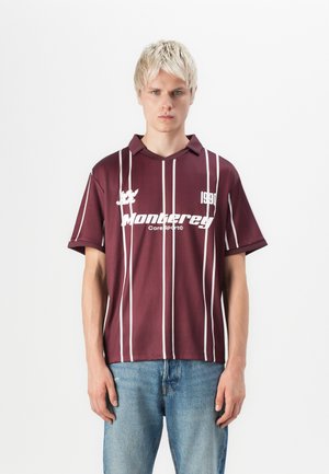 Bordeaux polo-shirt med hvide lodrette striber, korte ærmer og krave. Har "Monterrey" logo og "1990" detalje på forsiden.