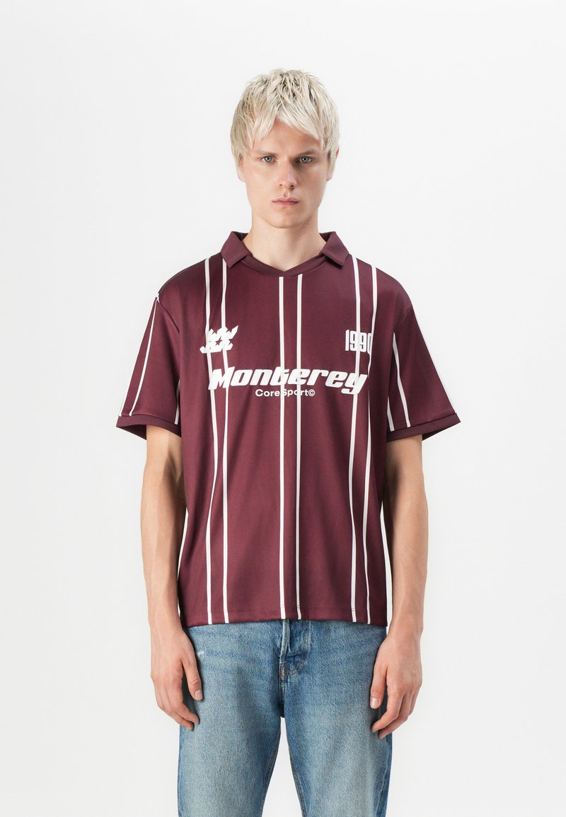 Burgunderfarget polo-skjorte med hvite vertikale striper, korte ermer og krage. Har "Monterrey" logo og "1990" detalj på framsiden.