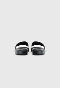 Et par sorte slide-sandaler med tykke teksturerede såler og brede stropper, vist fra bagsiden på en ensfarvet hvid baggrund.