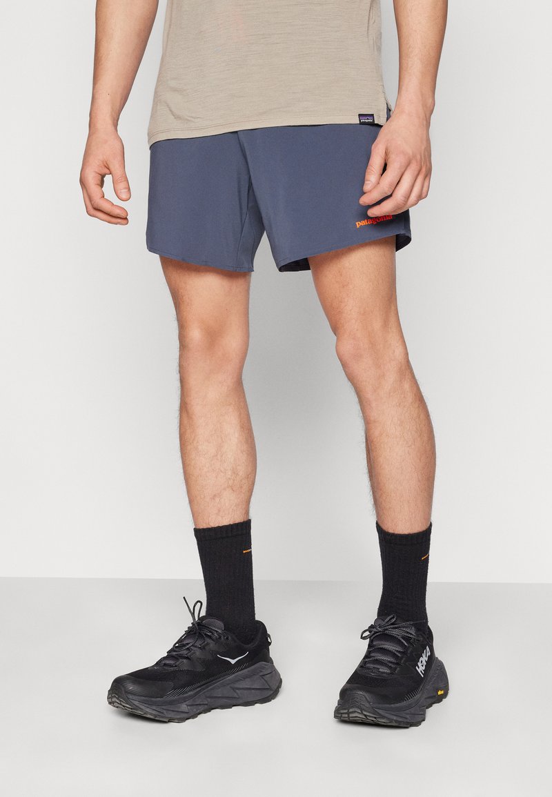 Navy athletic shorts with an orange logo, paired with black socks and black running shoes featuring a textured sole and chunkier design.