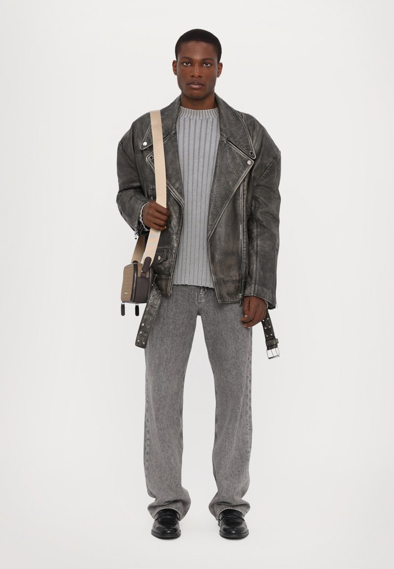 Svart skinn mc-jakke, grå ribbestrikket genser, grå jeans og svarte sko. Holder en liten crossover-veske med beige stropp.