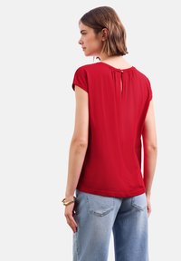 Blouse rouge à manches courtes avec un col arrondi et une petite ouverture dans le dos. Tissu doux, coupe décontractée, associée à un jean taille haute bleu clair.