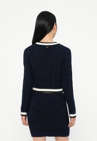 Abito in maglia di colore blu navy con accenti in bianco e nero a righe, tessuto texturizzato, design corto, maniche lunghe e dettaglio logo sul retro.