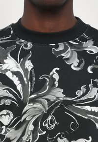 Felpa nera con un motivo floreale bianco e designs toccanti, colletto a girocollo a coste e una texture di tessuto morbido.