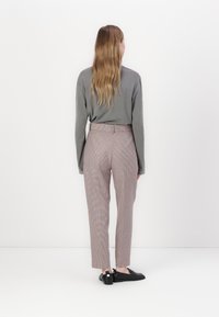 Camisola cinza de manga longa combinada com calças ajustadas de padrão xadrez em tons de rosa e castanho. Sapatos pretos com detalhes brancos completam o visual.