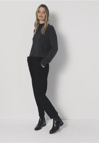 Maglione grigio scuro corto, pantaloni neri a sigaretta e stivaletti neri alla caviglia. Tessuto liscio, design minimalista, tasche laterali sui pantaloni.