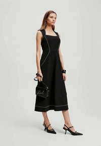 Mustat hihattomat mekot, joissa on valkoista ommeltua yksityiskohtaa, keskipitkä pituus, sileä kangas. Mukana musta laukku, jossa on kaunokirjoitettu logo, ja kärkitossut.