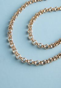 Close-up of a twisted gold chain necklace with interlocking oval links on a light blue background.
