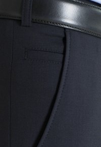 Dunkelblaue Hosen zeichnen sich durch ein schlankes Design mit flachem Bund, subtilen Taschenmerkmalen und glatter Stofftexture aus. Ein schwarzer Ledergürtel ist im Lieferumfang enthalten.