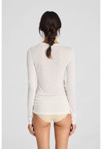 Top a maniche lunghe in crema chiaro con un motivo testurizzato, caratterizzato da un scollo rotondo e un design aderente, abbinato a pantaloni beige chiaro.