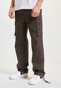 Pantalones cargo en un color verde oliva oscuro, con múltiples bolsillos laterales, diseño de pierna recta, material de algodón, combinados con zapatillas blancas que tienen un logotipo negro.