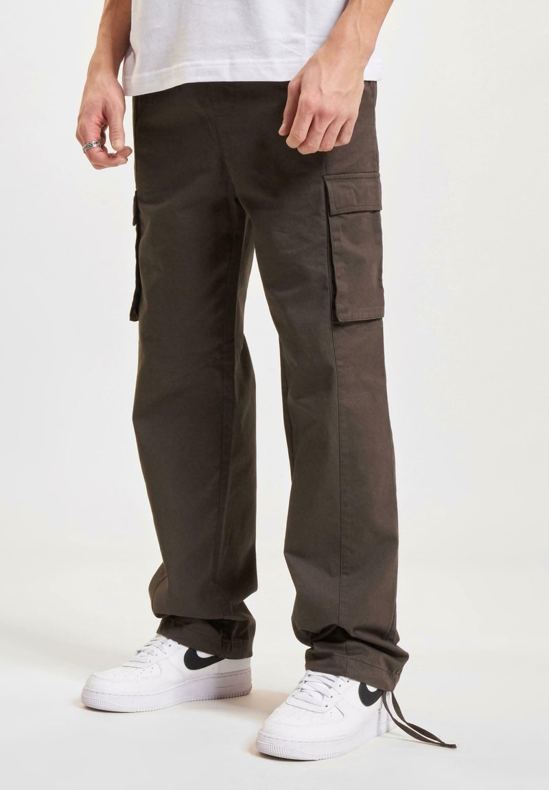 Pantalones cargo en un color verde oliva oscuro, con múltiples bolsillos laterales, diseño de pierna recta, material de algodón, combinados con zapatillas blancas que tienen un logotipo negro.