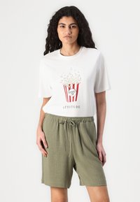 Witte t-shirt met een popcornafbeelding in rood en wit met tekst; gecombineerd met losse olijfgroene shorts met een verstelbare trekkoord.