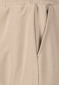 Beige Baumwoll-Jogginghose mit elastischem Bund und Seitentaschen. Der Stoff hat eine glatte, leicht strukturierte Oberfläche.