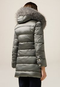 Giacca a vento grigia con cappuccio foderato in pelliccia, caratterizzata da cuciture orizzontali e dettagli con bottoni a pressione sulle maniche. Texture liscia e lucida.