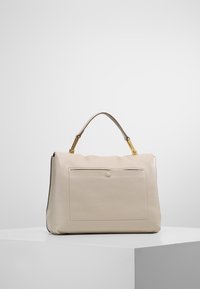Sac à main en cuir beige avec une texture lisse, une poche avant plate, des garnitures dorées et une seule anse supérieure.