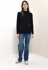 Schwarzer Strickpullover mit hohem Kragen, kombiniert mit hellblauen ausgestellten Jeans und weißen Sneakers. Einfaches Design mit strukturierter Optik.