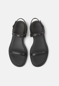 Czarne skórzane sandały z regulowanym paskiem, płaską podeszwą i minimalistycznym wzornictwem. Gładka tekstura z wytłoczonym logo w okolicy pięty.