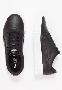 Baskets en cuir synthétique noir avec semelles en caoutchouc blanches, présentant un design à lacets, un détail perforé sur les orteils et une marque subtile sur la languette.