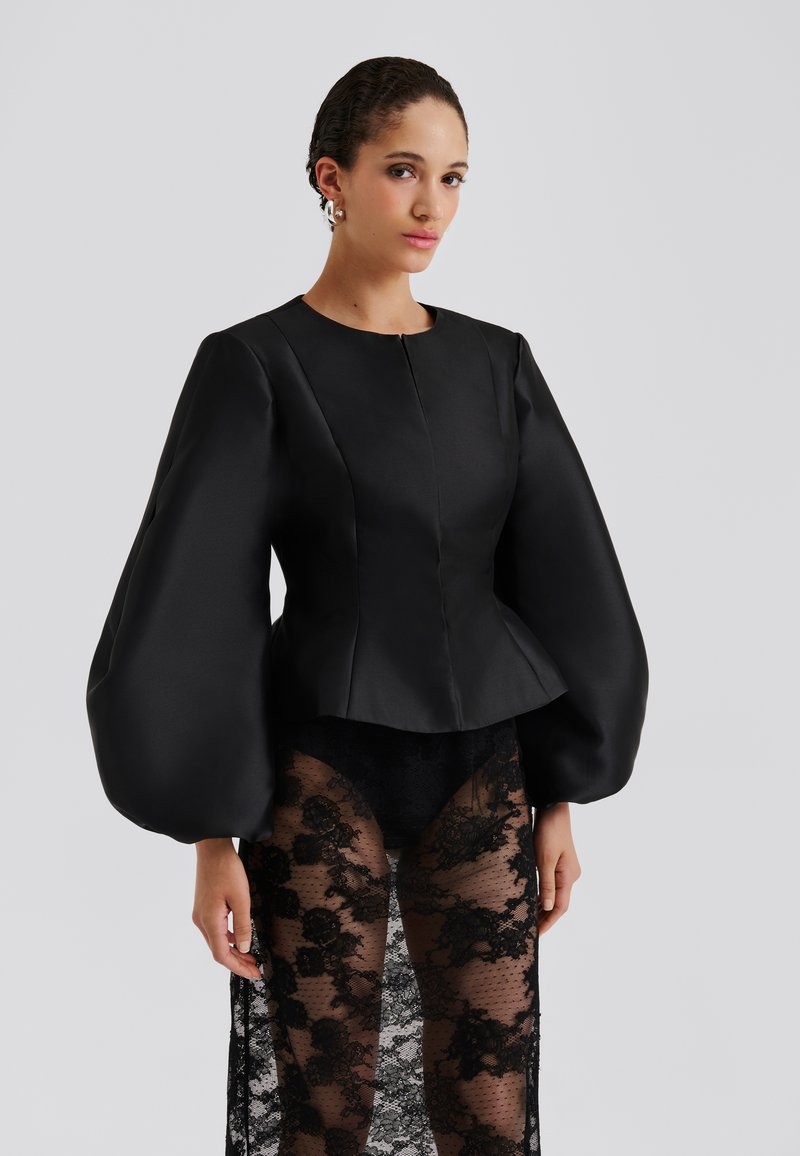 Μαύρη σατέν μπλούza με peplum και φουσκωτά μανίκια, συνδυασμένη με διάφανα lace παντελόνια με λουλουδάτα μοτίβα και πουά.