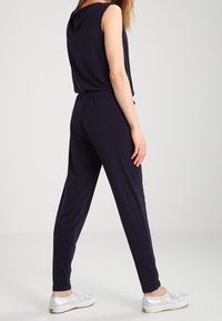 Mono de marinero con diseño sin mangas, banda elástica en la cintura, piernas ajustadas y tejido suave. Llevado con zapatillas plateadas y un aspecto minimalista.