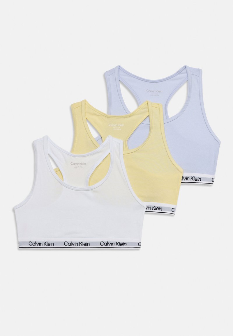 Τρία crop tops Calvin Klein με racerback, σε λευκό, κίτρινο και ανοιχτό μπλε, το καθένα με ελαστικές ταινίες με το λογότυπο στο κάτω μέρος.