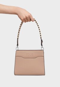 Beżowa skórzana torebka o teksturowanej powierzchni, z plecionym paskiem w kolorze kremowym i brązowym, z wytłoczonym logo z przodu oraz srebrnym okuciem.