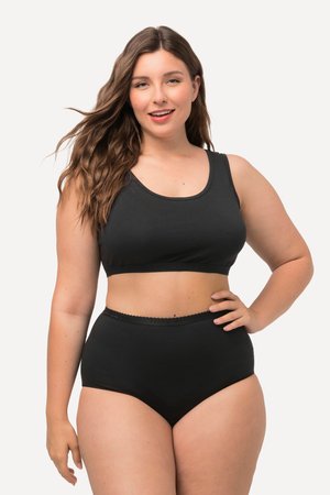 Smilende kvinde med langt brunt hår poserer med hånden på hoften iført sort sports-bh og trusser med højtaljet pas mod hvid baggrund.