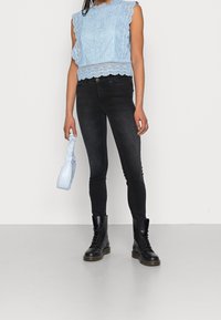 Ljusblå spetsblus med böljande kanter, kombinerad med svarta smala jeans och svarta kängor. Bär en liten ljusblå väska.