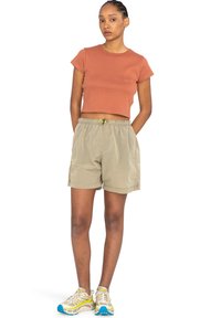 Camiseta corta de color marrón claro, pantalones cortos de cuadros en tonos beige con cintura elástica y cordón, combinados con zapatillas beige con detalles en azul.