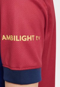 Crvena sportska majica s teksturiranim materijalom, plavi naglasci na manžetama i istaknuti žuti logo "AMBIILIGHT tv" na rukavu.