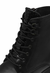 Bottine montante en cuir noir à lacets, avec languette texturée à motif peau de serpent et œillets en métal, dotée d'une doublure intérieure chaude.