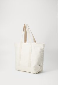 Borsa a tracolla in tela di colore avorio, con due ampie maniglie in tessuto, forma rettangolare e dettagli di cucitura minimali sui lati.