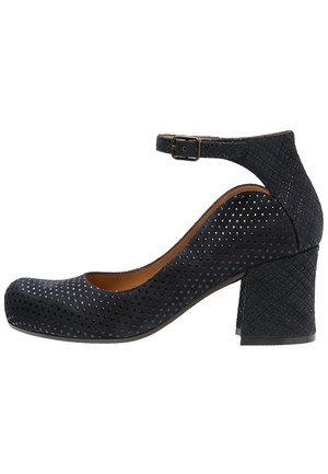 Chaussure noire texturée à petit talon bloc avec bride de cheville et boucle, bout arrondi et petit motif de points perforés sur le dessus.