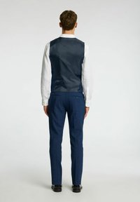 Mornarski hlačnik z gladko teksturo, v kombinaciji z krojenimi modrimi hlačami. Hlačnik ima preprost dizajn in gumbe na hrbtu. Bela srajca spodaj.