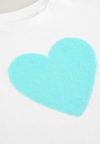 Weißes T-Shirt mit einem großen, strukturierten Herzdesign in Hellblau, aus weichem Material mit erhabenen, schuppenartigen Mustern.