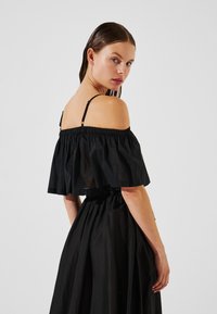 Top nero scollato con rouches sul collo e spalline sottili, abbinato a una gonna nera fluida con una cintura elastica.